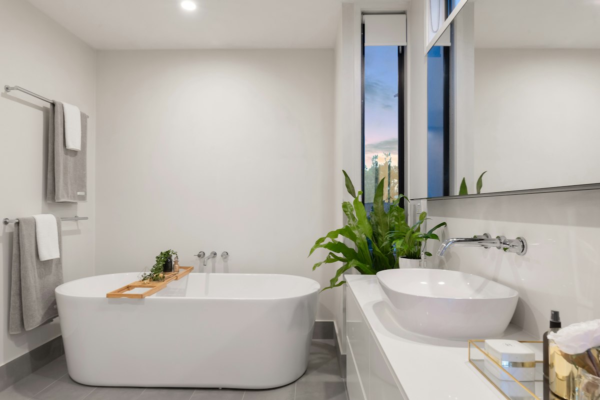 Modern soaking tub with bamboo bath caddy tray, vessel sink, and floating white vanity.