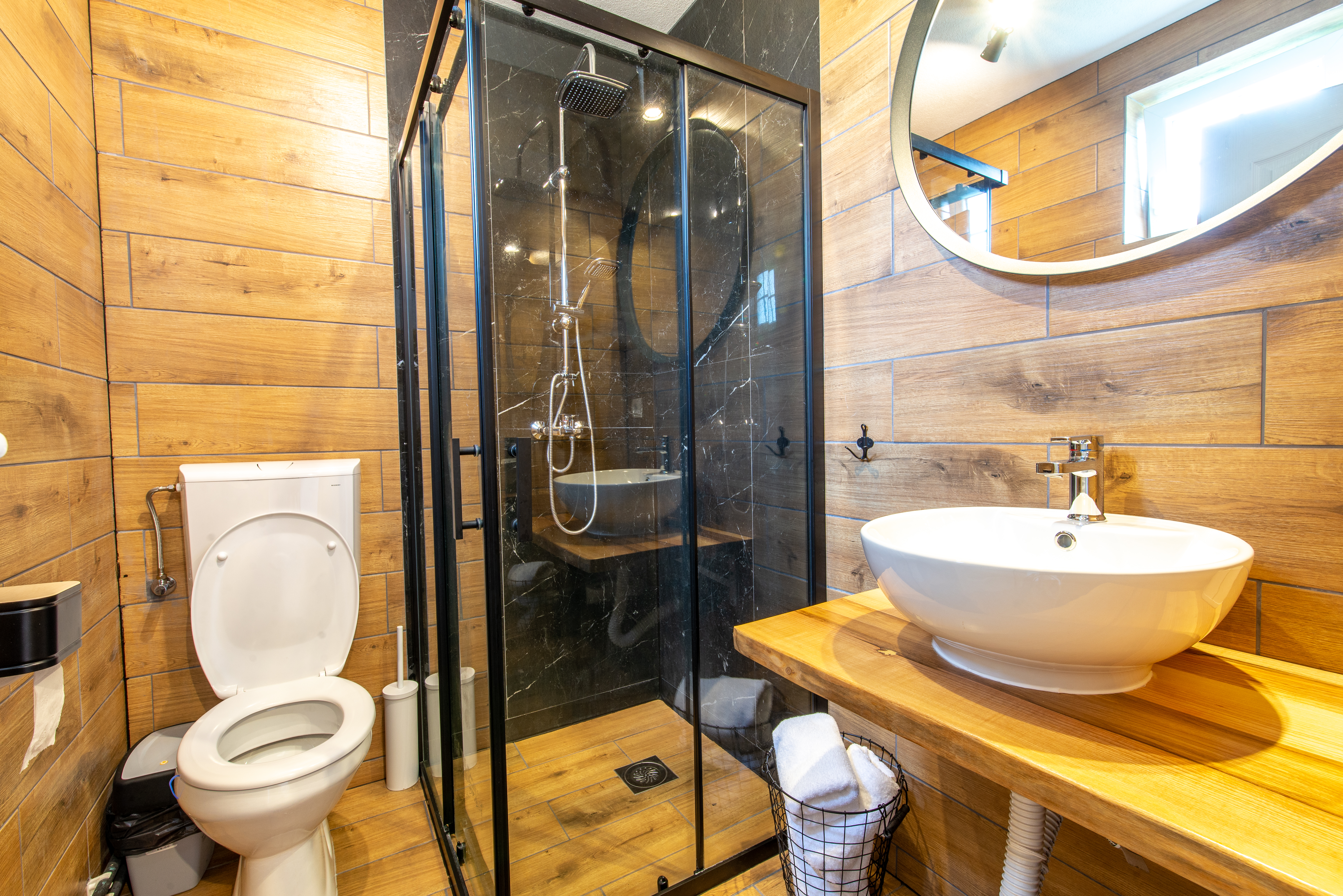 Warm wood-tile bathroom with level-entry shower floor, black framed glass enclosure, and floating vanity.