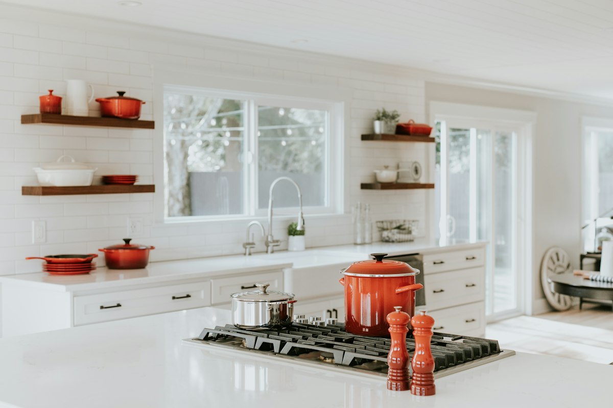 Sunlit kitchen with white quartz island, farmhouse sink, floating wooden open shelves, and subway tile.